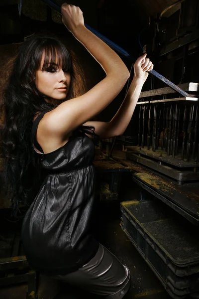 Sexy brunette model in an old workshop holding a pole — Stock Photo, Image