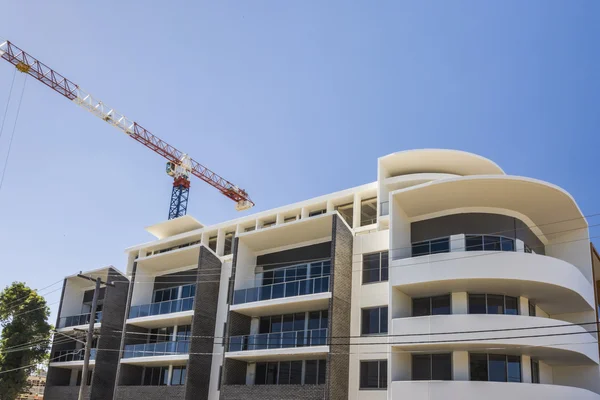 Acabamento de edifício moderno com um guindaste sob o céu azul — Fotografia de Stock