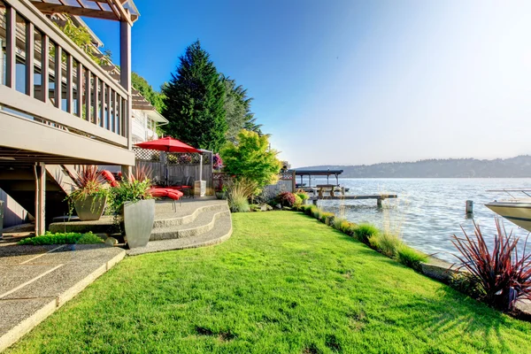 Furnished back patio with red chairs, grass, and water view. Wat — Stock Photo, Image