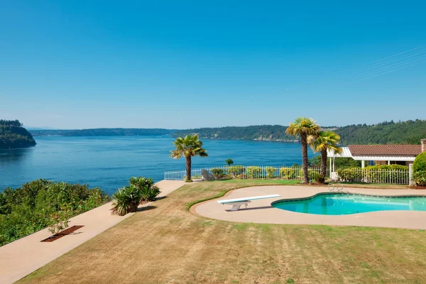 Piscine à la maison de luxe au bord de l'eau avec grande pelouse et vue o — Photo