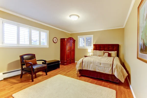 Cozy large guest room with suede brown bed and armor, hardwood floors and beige walls. — Stock Photo, Image