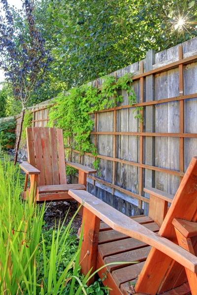 Kleine groene omheinde achtertuin met houten stoelen. — Stockfoto