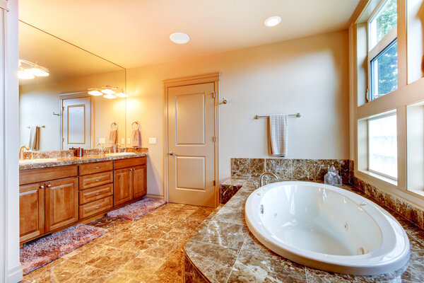 Luxury bathroom interior with tile floor. White bath tub with brown granite tile trim.
