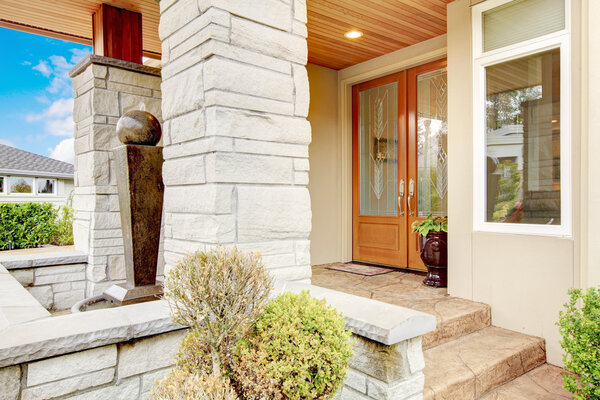 Luxury house entrance porch with stone column trim and stained wood door.