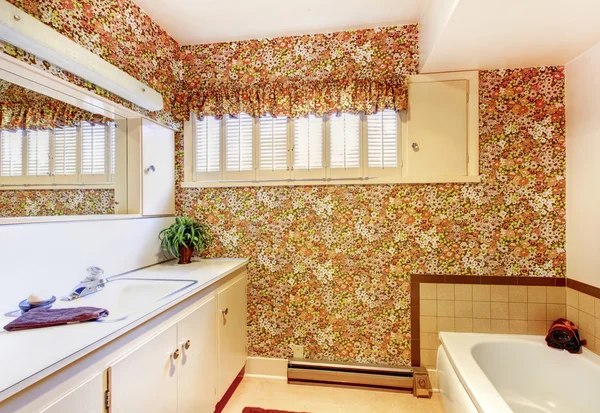 Baño antiguo con fondo de pantalla de patrón floral, gabinetes blancos y bañera . — Foto de Stock