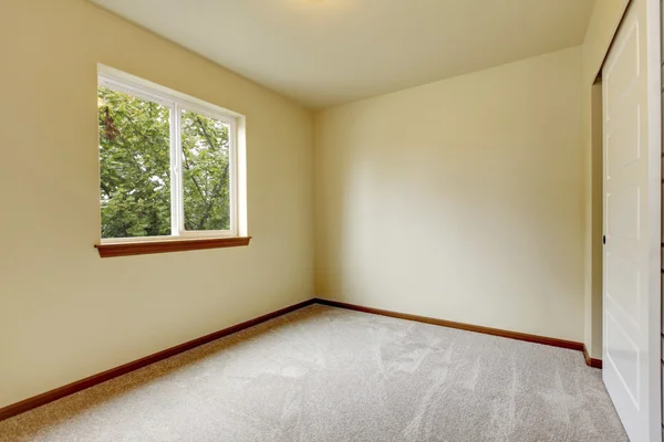 Habitación pequeña y luminosa con suelo de alfombra, ventana y paredes de marfil . — Foto de Stock