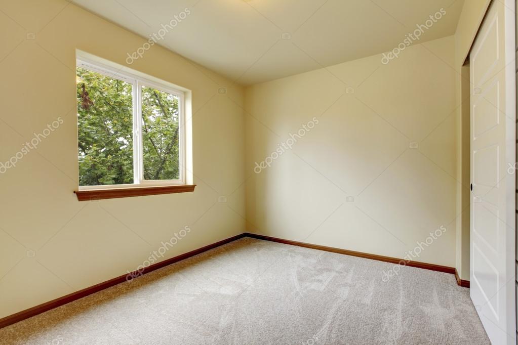 Bright small empty room with carpet floor, window and ivory walls