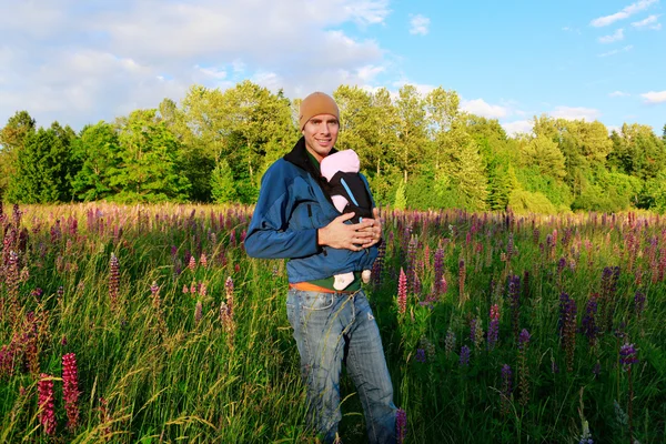 Young father holding a baby girl in a sling. — Stock Photo, Image