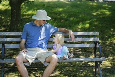 Yardımsever baba çocukla ahşap bir bankta oturur. 
