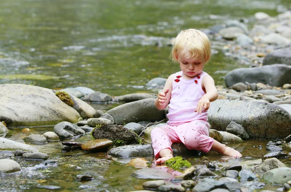 Sporca bambina in un abito rosa seduto sulle rocce nel fiume — Foto Stock