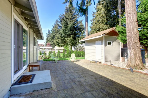 Backyard deck with tile floor and two green chairs. View of small shed. — Stock Photo, Image