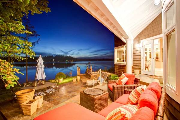 Lujosa casa exterior con impresionantes vistas al agua y sofá de mimbre con almohadas rojas en la cubierta del patio trasero .. — Foto de Stock
