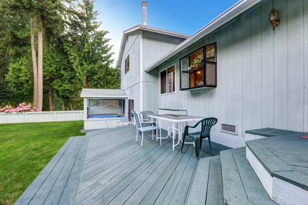 Blauwe walkout dek met patio tafel en stoelen. Uitzicht op de hot tub. — Stockfoto