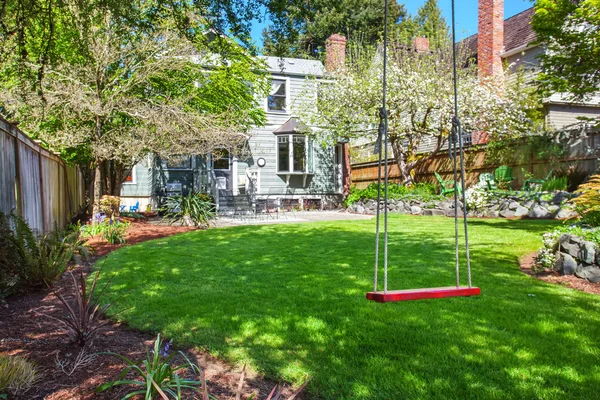 Kinderschommel zitten in de achtertuin tuin met goed onderhouden gazon. — Stockfoto