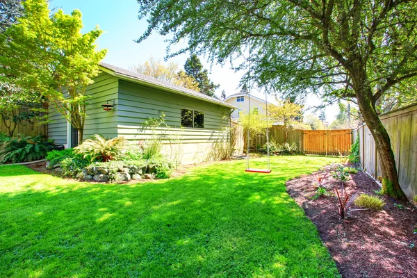 Fenced back yard with child\'s swing sit and green shed behind.