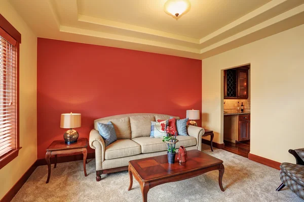 Acogedora sala de estar con sofá beige antiguo y pared roja detrás . —  Fotos de Stock
