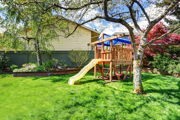 Vista del parque infantil en el jardín verde del patio trasero con abedules y cama de flores . — Foto de Stock