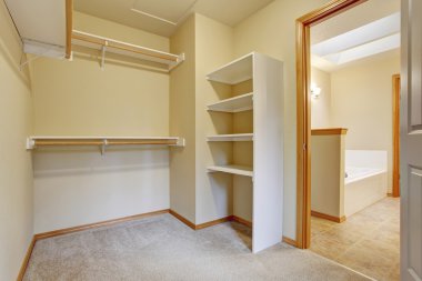 Empty walk-in closet with wood shelves, beige carpet floor. clipart