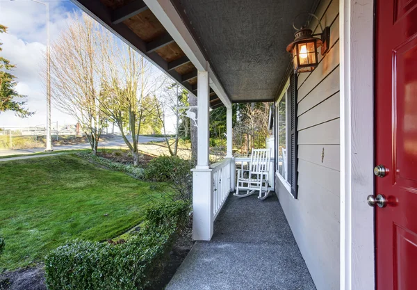 Small covered porch with white rocking chair and red front door. — Stock Photo, Image