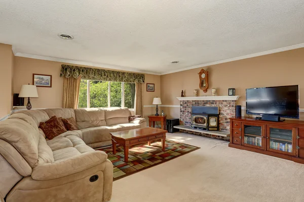 Sala de estar em tons cremosos com sofá canto e lareira de tijolo . — Fotografia de Stock
