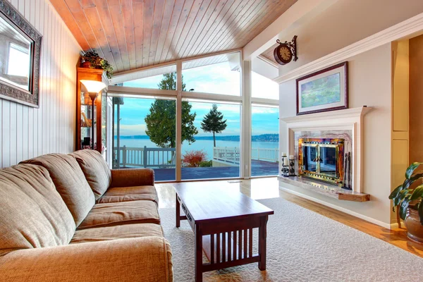 Impresionante interior de la sala de estar con techo de madera inclinada y vista al agua . —  Fotos de Stock