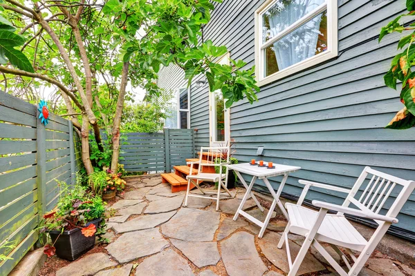 Small fenced back yard with stone floor and chairs. — Stock Photo, Image