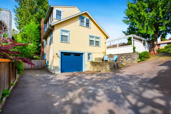 Esterno di casa gialla con porta del garage blu e strada asfaltata — Foto Stock