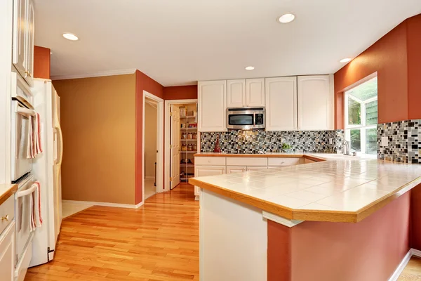 Белый интерьер кухонной комнаты с кафельной столешницей и деревянным полом . — стоковое фото