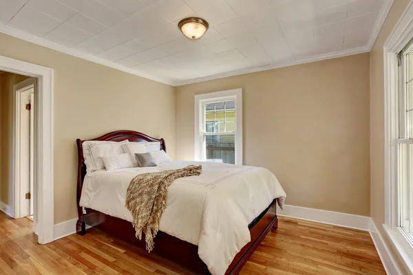 Empty bedroom interior with white bedding and hardwood floor.