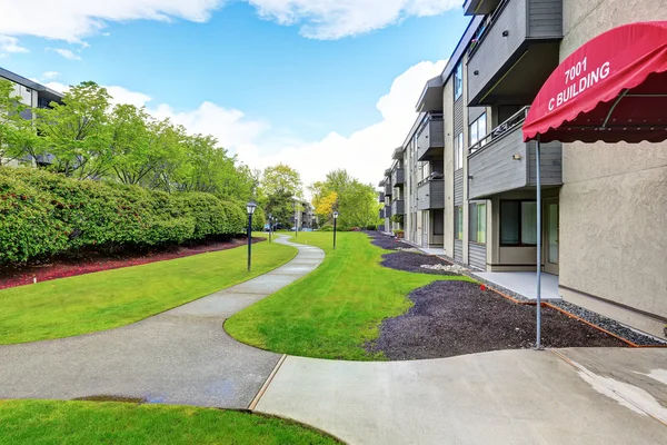 Stor beige bostadshus med tre våningar och balkonger. Välskött gräsmatta — Stockfoto