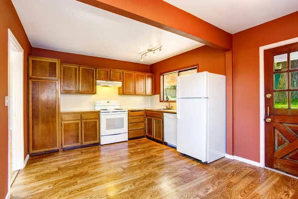 Kuchyňský pokoj s wodenskými skříňkami, podlahou z tvrdého dřeva a červenými stěnami. — Stock fotografie