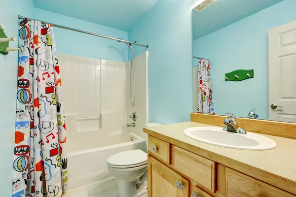 Kids bathroom in blue tones with wooden cabinets and colorful shower curtain. — Stock Photo, Image