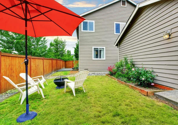 Inhägnad bakgård uteplats med öppnat rött paraply, välskött gräsmatta — Stockfoto