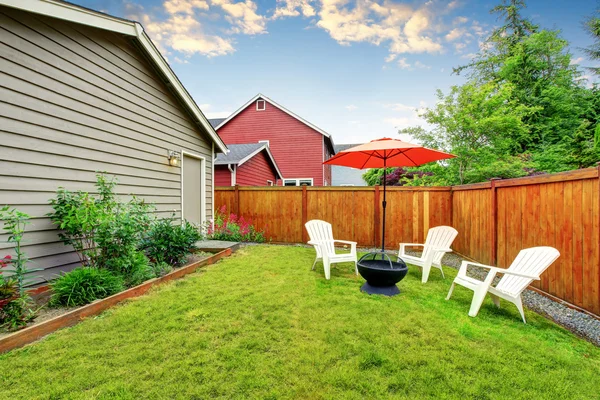 Fenced backyard patio with opened red umbrella , well kept lawn — Stock Photo, Image