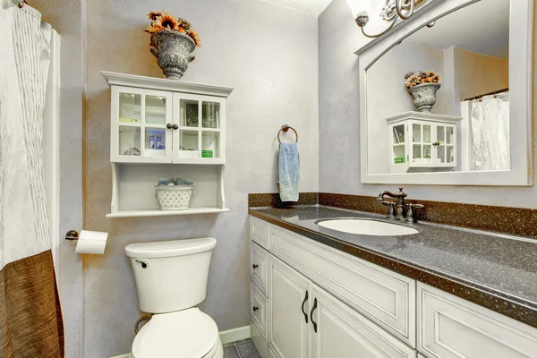 Интерьер небольшой ванной комнаты с белыми шкафами, гранитной столешницей и туалетом . — стоковое фото
