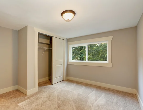 Tomt rum med mjuk beige mattgolv, fönster och garderob. — Stockfoto