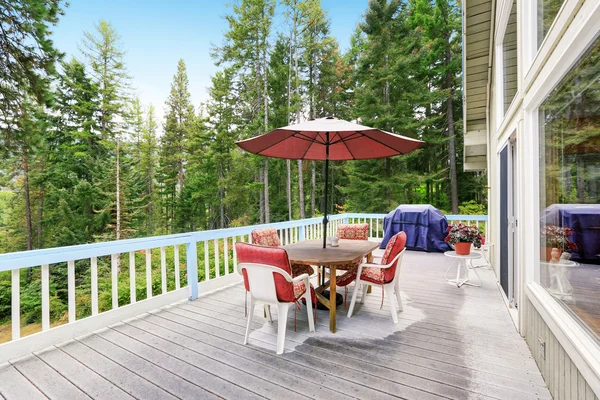 Wooden walkout deck after rain. Furnished with red chairs and table with umbrella — Stock fotografie