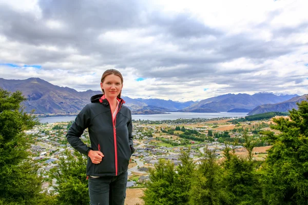 Mujer joven y bonita se aloja en la montaña con vista panorámica del lago Wanaka ciudad en la parte posterior Nueva Zelanda —  Fotos de Stock