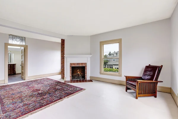 Puste wnętrze tradycyjnego pokoju w odcieniach bieli z ceglanym kominkiem i dywanem — Zdjęcie stockowe