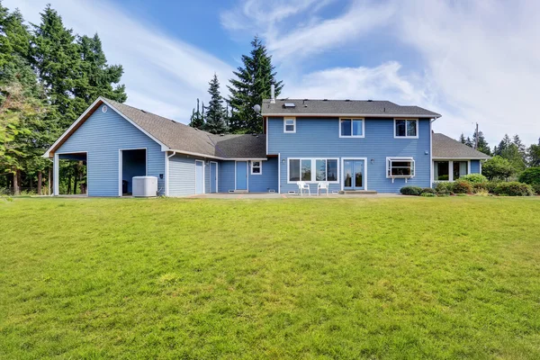 Blue house backyard with concrete floor patio area and well kept garden.