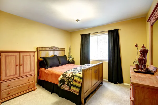 Zářivě žlutá ložnice s vyřezávanou dřevěnou postel — Stock fotografie