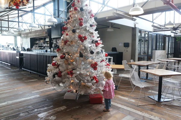 Little girl is looking at white Christmas tree with red present. — Stock Photo, Image