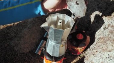 Taşınabilir gaz ocağında bir kahve makinesi. Adam kahve makinesinin kapağını açıyor. Yürüyüşte kahve yapmak.