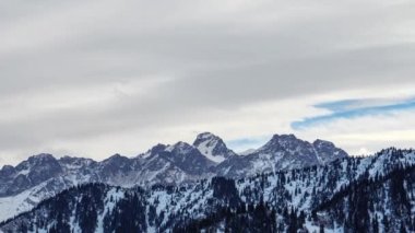 Bulutlar karlı dağların tepelerinde hareket eder. Kışın dağ manzaraları. Orta Asya 'daki Tian Shan dağlarında Almaty yakınlarındaki kayalar ve buzla panoramik dağ manzarası. Zaman Uygulaması