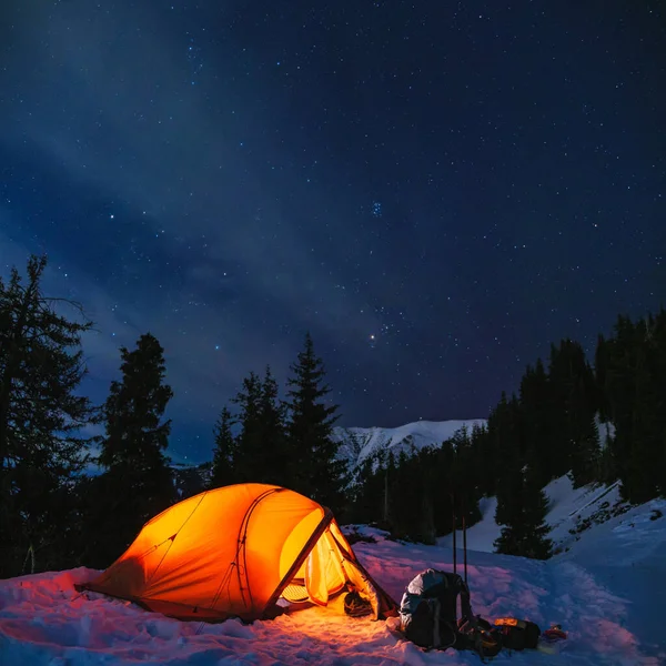 Mountain winter night landscape with orange tent. Hiking with an overnight stay in the mountains in winter