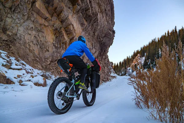 A winter traveler on a bicycle in the mountains climbs to the top along the road among the steep cliffs. Winter travel. Turgen gorge, Kazakhstan