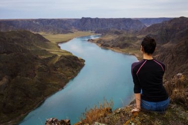 Kız güzel nehir kanyonunun uçurumunda oturuyor. Arkadan bak. Ili Nehri. Kazakistan