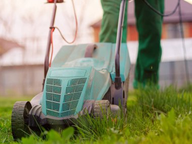 Çim biçme makinesi arka bahçede yeşil çim biçiyor. Yaz ve bahar mevsimi bahçe işleri.
