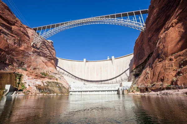 The Glen Canyon Dam holding back Lake Powell and the Glen Canyon Bridge with a clear blue sky background as seen from the surface of the Colorado River near Page, Arizona.