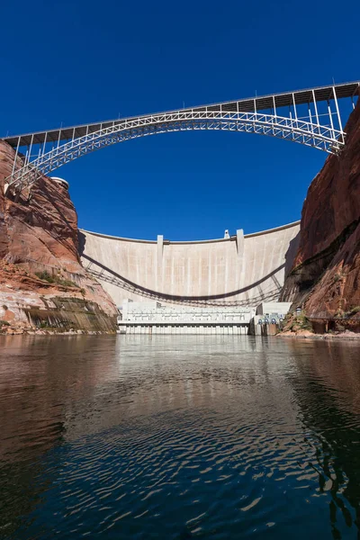 The Glen Canyon Dam holding back Lake Powell and the Glen Canyon Bridge with a clear blue sky background as seen from the surface of the Colorado River near Page, Arizona.